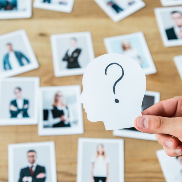 cropped view of man holding paper with human head and question mark near photos